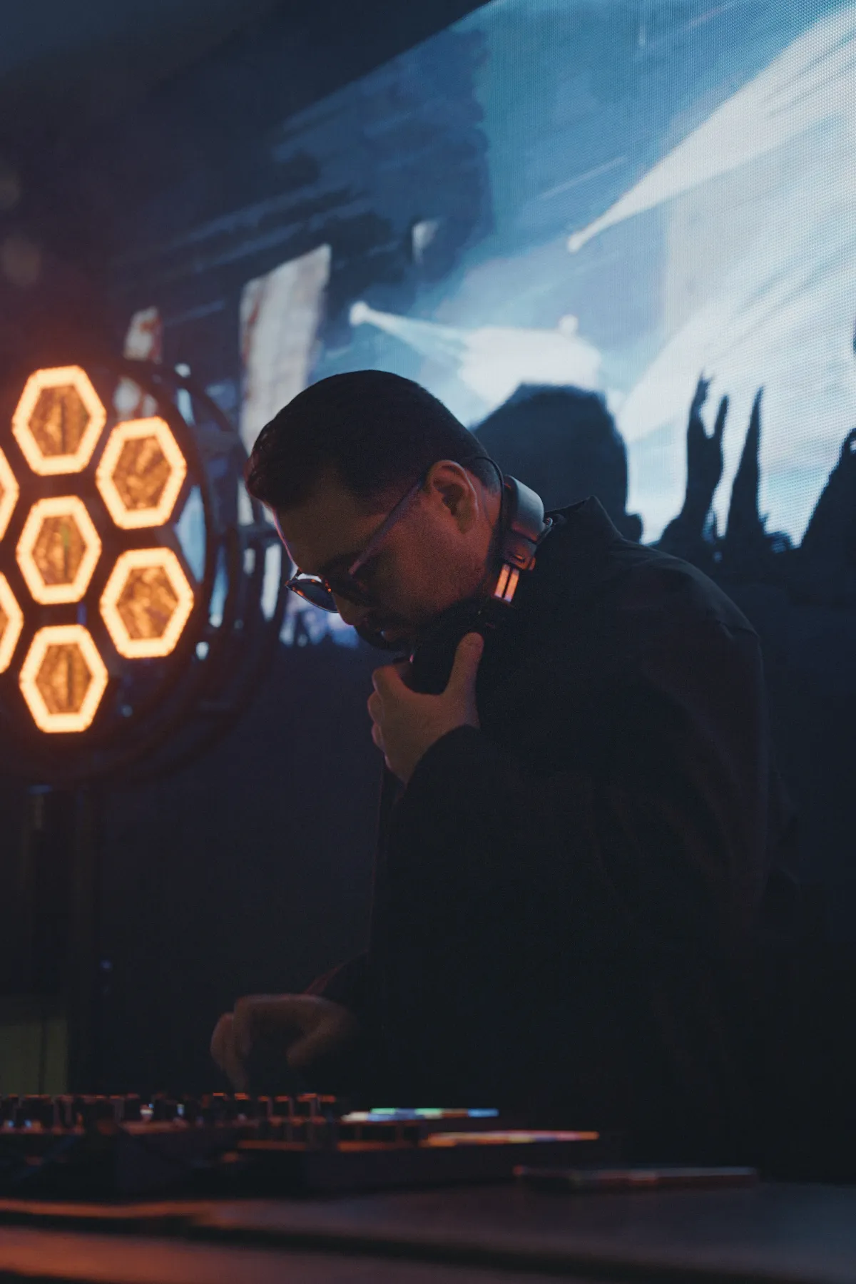 DJ Mehras behind the decks, honeycomb stage lights glowing beside him
